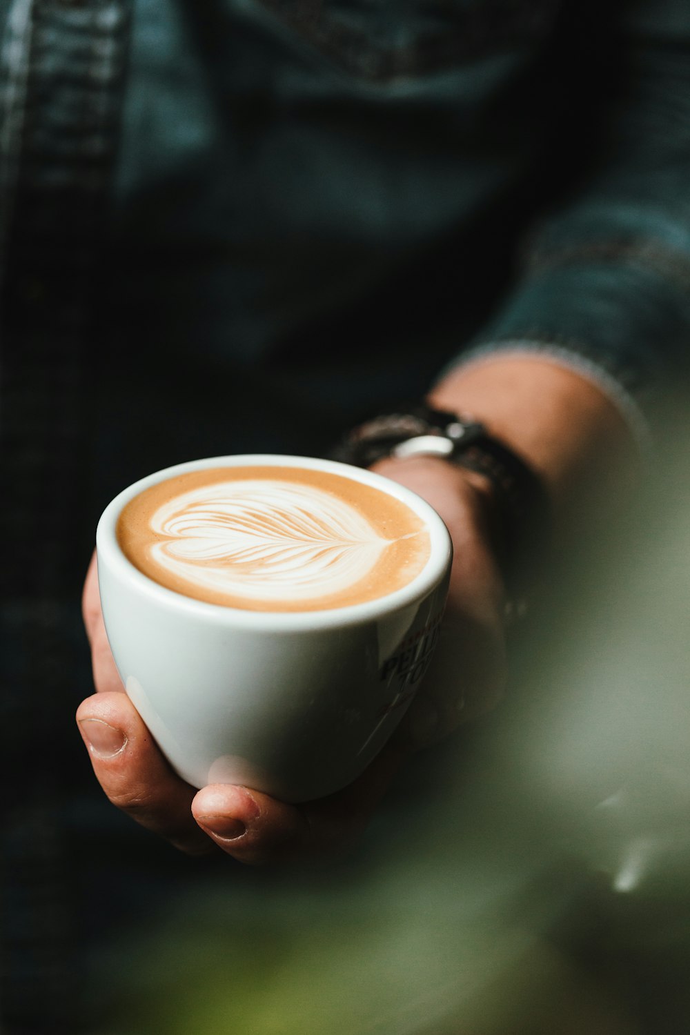 A hand holding a cappuccino with latte art, against a dark background.
