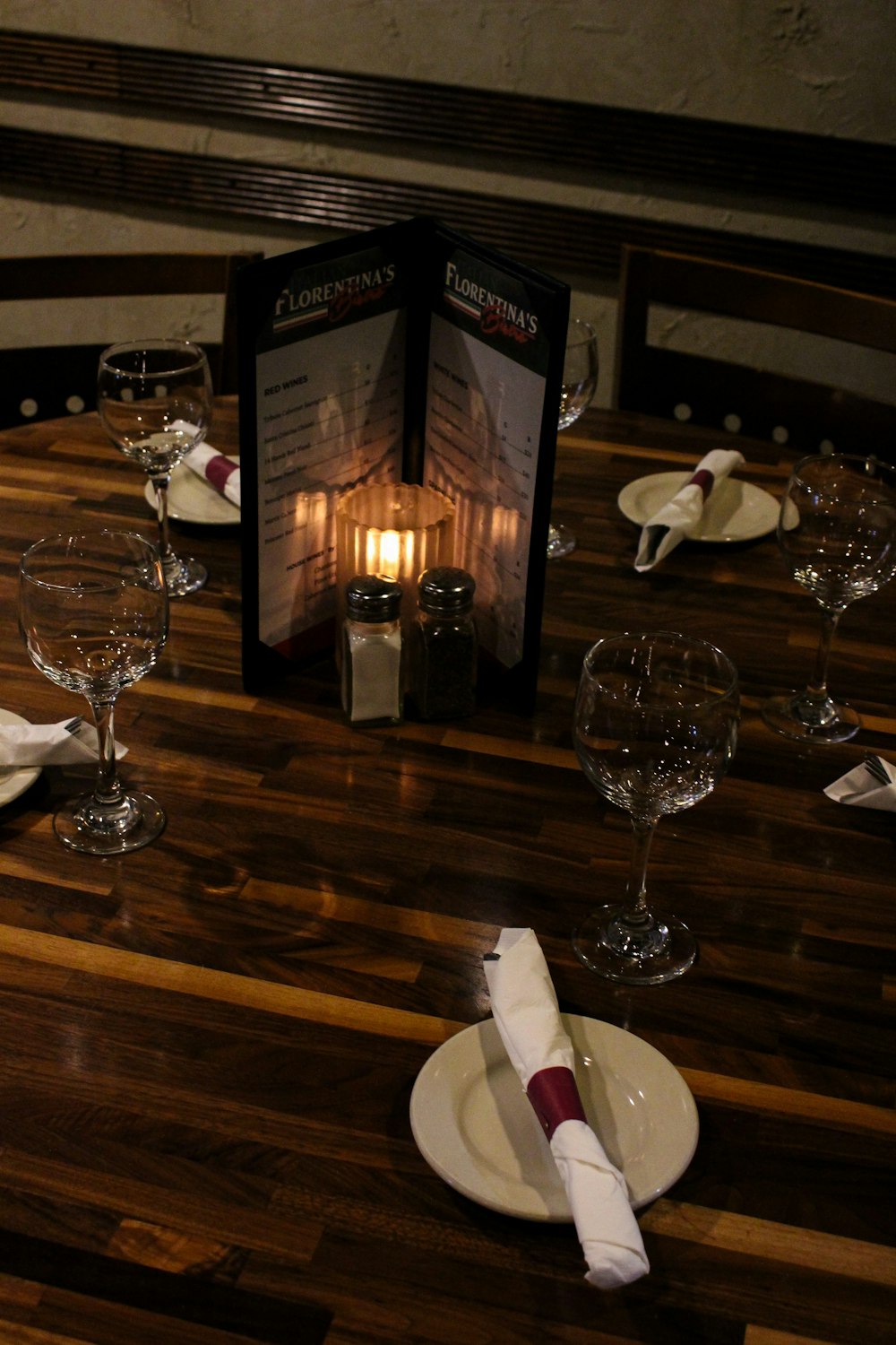 A candlelit restaurant table set with wine glasses, folded napkins and menus.